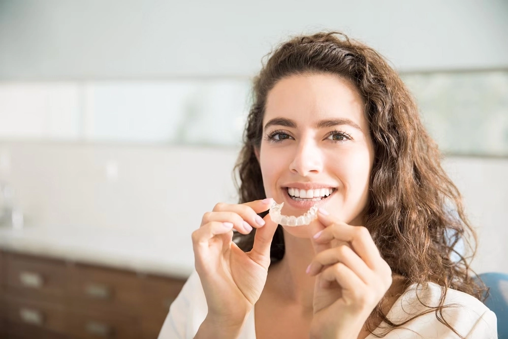 Smiling woman holding clear aligners during her Invisalign Ajax treatment.